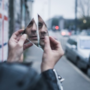 Punk guy looking at himself in a shattered mirror in the city streets