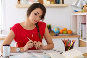 47986718 - female student at workplace portrait holding pen and looking in textbooks studying. woman writing letter, list, plan, making notes, doing homework. education, self development and perfection concept